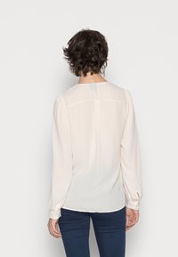 Lyserød bluse med lange ærmer, blødt stof, samlet skulderdetalje og knappede manchetter, stylet med mørkeblå jeans.