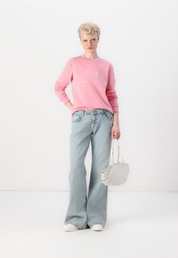 Light pink sweatshirt with text print, paired with light blue flared jeans and a small white handbag. Overall casual look with white sneakers.