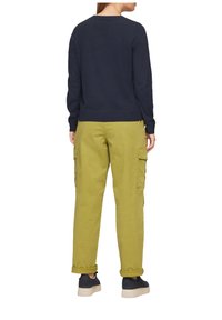 Maglione blu navy con scollo rotondo, abbinato a pantaloni cargo verde oliva con tasche laterali e orli risvoltati, indossati con scarpe scure.
