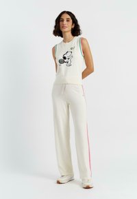 Maglione senza maniche crema con accenti verdi e rosa, caratterizzato da una grafica di Snoopy nera. Pantaloni abbinati crema con strisce laterali rosa.