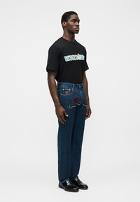 Μαύρο γραφικό μπλουζάκι με την επιγραφή "ICEDREAM", μπλε τζιν με κόκκινη και χάντρες κεντήματα, συνδυασμένο με μαύρα δερμάτινα παπούτσια.