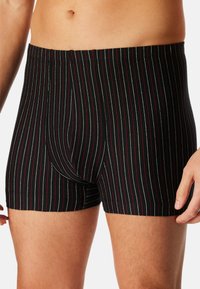 Boxer neri a righe, con sottili linee verticali rosse e bianche. Realizzati in tessuto morbido, con design aderente e apertura frontale.