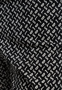 Tissu noir avec un motif répétitif de lettres majuscules blanches disposées en diagonale formant le mot « STOLDS » à plusieurs reprises.
