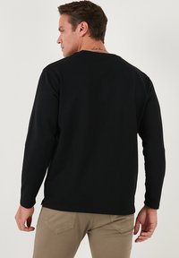 Maglietta nera a maniche lunghe con scollatura rotonda. Tessuto liscio con un leggero lucido, silhouette aderente e spacchi ai lati dell'orlo.