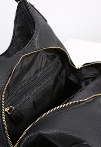 Svart läderväska med en texturerad yta, gulddragkedja och ett foder med en dragkedjefick och organisatoriska fack.