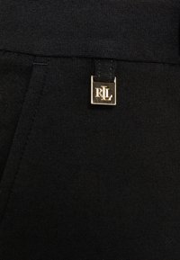 Svart tyg med en slät textur har en sytt etikett med guldhårdvara som visar "R L". Designen är enkel och elegant.