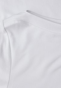 Hvid bomuldsstof med en glat tekstur, med buede nakkesømme og skuldersømme, der viser et rent og minimalistisk design.