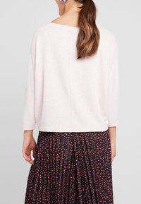 Helles rosa, locker sitzendes Sweatshirt mit Dreiviertelärmeln, weicher Textur und weitem Ausschnitt, kombiniert mit einem schwarzen Rock mit roten Mustern.