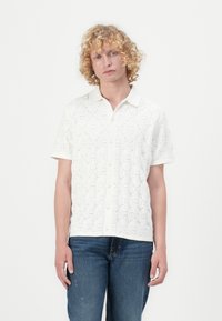 Witte blouse met korte mouwen, voorzien van een textuurpatroon met vierkante ontwerpen en kleine uitsparingen, knoopsluiting aan de voorkant en zachte stof.