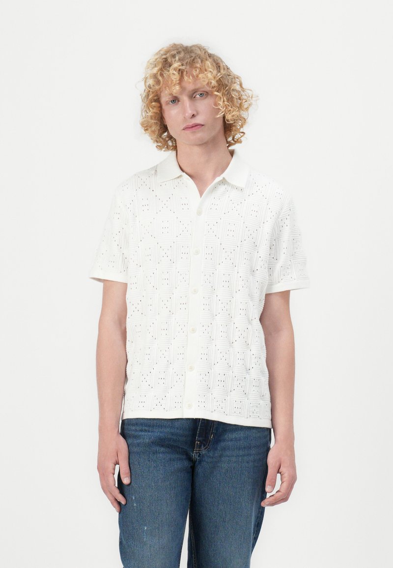 Witte blouse met korte mouwen, voorzien van een textuurpatroon met vierkante ontwerpen en kleine uitsparingen, knoopsluiting aan de voorkant en zachte stof.