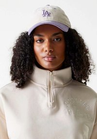 Felpa beige con zip a metà colletto e testo in rilievo "Dodgers 1958". Cappello in corduroy chiaro con logo LA in viola e cuciture decorative.