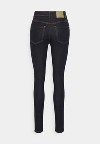 Jeans skinny azul escuro com uma textura suave, acentuados por costuras amarelas contrastantes e dois bolsos traseiros. Etiqueta de tecido na cintura.