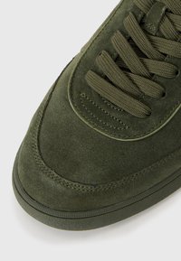 Sneaker din suede verde măsliniu, cu vârf rotund, suprafață texturată, șireturi plate și cusături contrastante. Talpă din cauciuc ușoară.