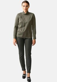 Olivegrünes Rollkragenbluse aus glattem Material, kombiniert mit dunkelgrünen, figurbetonten Hosen und schwarzen Loafern mit Kettenakzenten.