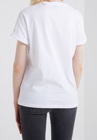 Vit bomulls T-shirt med rullade korta ärmar, avslappnad passform och rundad halsringning, i kombination med mörkgrå jeans. Enkel och klassisk design.