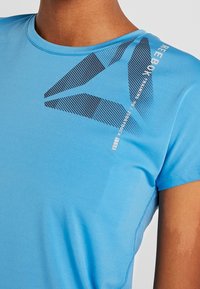 Blå kortärmad idrottströja av slät tyg, med en grafisk design i mörkblått och vitt på framsidan och rund halsringning.