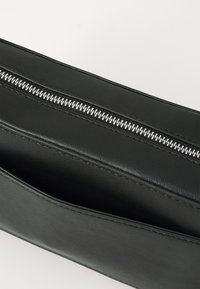 Black leather clutch bag with a silver zipper along the top. Textured surface and clean lines, featuring a slim, rectangular shape.