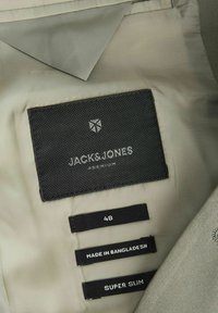 Μαύρες ετικέτες υφάσματος σε μπεζ ρούχα που δείχνουν την επωνυμία JACK&JONES PREMIUM, μέγεθος 48, κατασκευασμένο στο Μπαγκλαντές, υπερλεπτή εφαρμογή.