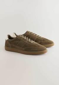 Braune Wildledersneaker mit niedriger Profilhöhe, mit strukturierten Seiten, runder Zehenform und beigen Akzenten an der Ferse und den Schnürsenkeln. Gerillte braune Sohle.