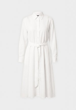 Balta su ilgomis rankovėmis marškinių stiliaus suknelė su apykakle, priekyje užsegama mygtukais ir audinio diržu, rišamu juosmens lygyje, pateikta ant vienspalvio fono.