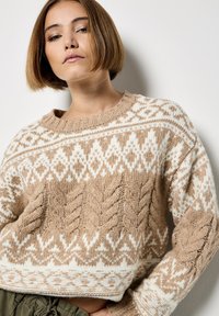 Beżowy sweter dziany o skróconym kroju, z wzorem w warkocze w różnych odcieniach kremu i brązu, okrągłym dekoltem i ściągaczami na rękawach.