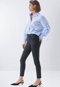 Camisa de hombre a rayas en azul claro y blanco, combinada con pantalones negros ajustados de cintura alta y cierre de doble botón.