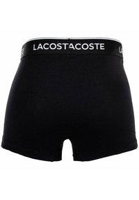 Svarta bomullskalsonger med bred midjeband som har vit "LACOSTE"-logotyp. Slät textur och en snug passform med benöppningar.
