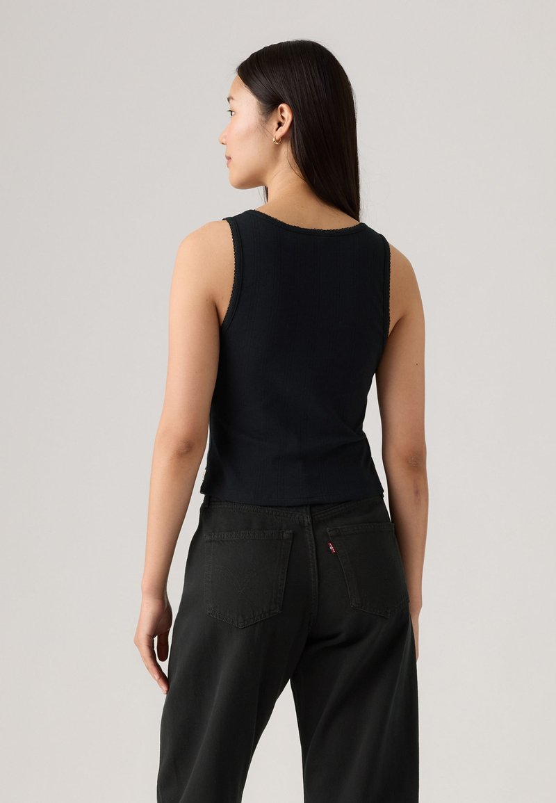 Schwarzes, geripptes Tanktop mit tailliertem Design, das einen gewellten Ausschnitt und schmale Träger hat, kombiniert mit hochsitzenden schwarzen Jeans.