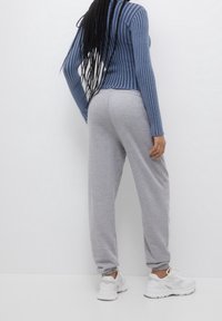 Grijze sweatpants met een elastische tailleband en verlaagde enkels, gecombineerd met een blauwe ribbelige lange mouw top en witte sport schoenen.