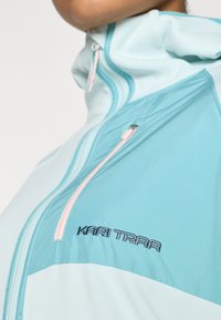 Φωτεινό γαλάζιο μπουφάν με ψηλό γιακά, διαθέτει ροζ φερμουάρ, κομψό σχέδιο και το λογότυπο Kari Traa εμφανίζεται έντονα στο πλάι.