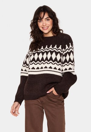 Brown knitted sweater with geometric white patterns, round neckline, and loose fit. Paired with brown trousers, featuring visible stitching.