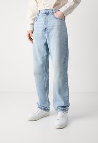 Lichtblauwe denim jeans met een rechte snit, featuring een hoge taille, vijf-pocket ontwerp en zichtbare stiksels, gecombineerd met witte sneakers.