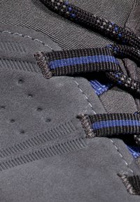 Zbliżenie na szary zamszowy but z czarnymi i niebieskimi paskowanymi pętelkami na sznurowadła oraz czarnymi sznurowadłami z niebieskimi akcentami.