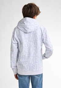 Witte hoodie met een patroon van herhaalde blauwe letters op de stof, voorzien van een trekkoordkap en geribde manchetten en zoom.