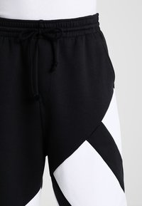 Black sweatpants with white diagonal accents, featuring an elastic waistband with a drawstring, made from a soft, textured material.