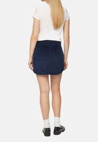 Marineblauwe corduroy mini-jurk met een lichte A-lijn, een achternaaddetail en een subtiele ribbeltextuur, gecombineerd met zwarte met studded schoenen.