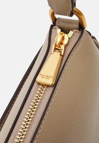 Beige synthetic handbag corner with a gold zipper, featuring a metal pull tab and a "kate spade" logo on a small tag.
