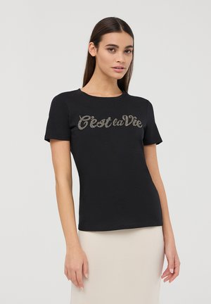T-shirt in cotone nero a maniche corte e scollo rotondo. Presenta il testo luccicante "C'est la Vie" in un font corsivo sul petto.