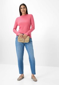 Roze geribbelde trui met lange mouwen, blauwe relaxte jeans, beige clutch met gespsluiting en lichtgrijze platte schoenen.