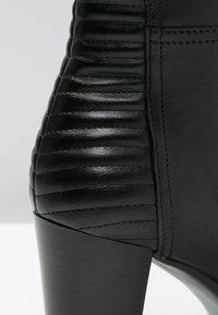 Talons de bottines en cuir noir avec détails côtelés rembourrés et coutures apparentes sur un fond lisse.
