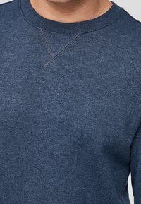 Suéter azul marino hecho de un tejido de punto texturizado. Presenta un escote redondo y un detalle de puntada en X en el pecho para mayor estilo.