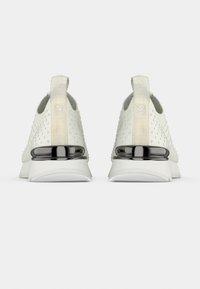 Chaussures de sport blanches avec un motif à pois et des accents métalliques, dotées d'un talon lisse et d'une semelle souple. Sans lacets visibles.