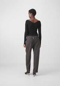 Haut noir à manches longues à côtes avec un large décolleté en V, associé à un pantalon taille haute gris anthracite avec un détail de boucle à l'arrière.