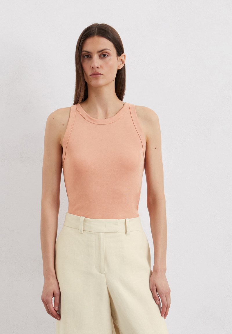 Peach-colored fitted tank top with a crew neck and sleeveless design, paired with cream wide-leg trousers. Smooth fabric texture.