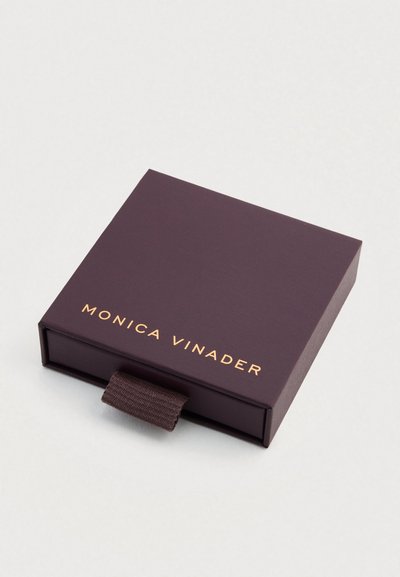 Cutie de carton mov cu finisaj mat, având un logo auriu „MONICA VINADER” pe partea frontală și o buclă din țesătură pentru deschidere.