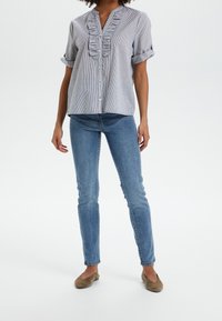 Randig skjorta med volangdetaljer, rullade ärmar; bärs med blå jeans och beige ballerinaskor. Slät tyg, avslappnad passform.