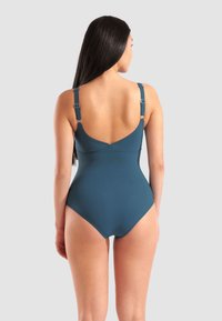 Jednodílné plavky v tmavě modrozelené barvě. Obsahují nastavitelné ramínka, nízký zadní díl a hladkou látku bez viditelných vzorů nebo textur.