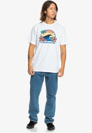 White cotton t-shirt featuring a colorful graphic of waves, palm trees, and flowers, paired with blue jeans and black shoes.