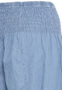 Tissu bleu clair avec une large ceinture élastique froncée et une texture douce plissée sous la ceinture.