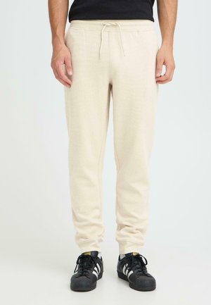 Beige, strukturierte Jogginghosen mit elastischem Bund und verstellbarem Kordelzug. Mit seitlichen Taschen und schmal zulaufenden Beinen. Kombiniert mit schwarzen Sneakern.